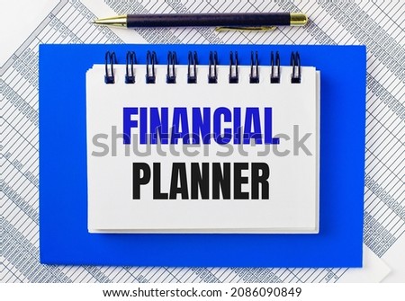 Against the background of reports on the desktop, a blue notepad. It has a pen and a white notebook with the text FINANCIAL PLANNER. Business concept