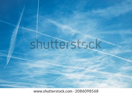 Airplane condensation trail or contrail with lines of clouds over blue sky background. High quality photo Royalty-Free Stock Photo #2086098568