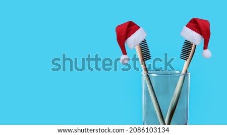 Christmas and New Year holiday background. Xmas greeting card. Bamboo eco friendly toothbrushes with santa hats on blue background 