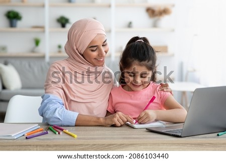 Doing Homework Together. Loving Muslim Mom Helping Her Little Daughter With Study While Sitting Together At Desk With Laptop Computer, Cute Preteen Girl Writing In Notepad And Smiling, Closeup