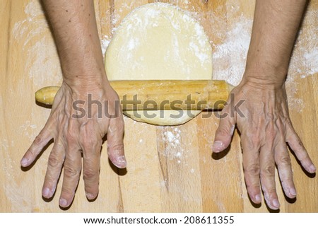 Hands with rolling kneading dough in foreground 