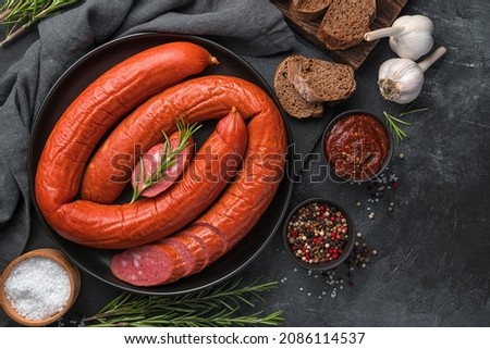 Smoked Krakow sausage with sauce, spices and fresh rosemary on a dark background. Top view, copy space.