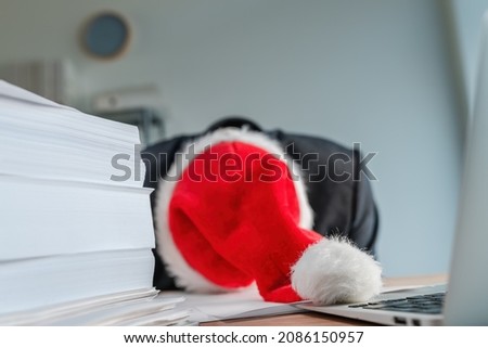 Tired and exhausted businessman with Santa Claus hat fell asleep over his office desk during Christmas season holiday, selective focus Royalty-Free Stock Photo #2086150957