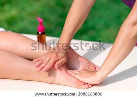 Massage of legs, female feet with oil outdoors. Close up photo of woman foot and therapist's hands of masseur massagist. Professional physiotherapist. Unrecognisable person is lying, relaxing on table