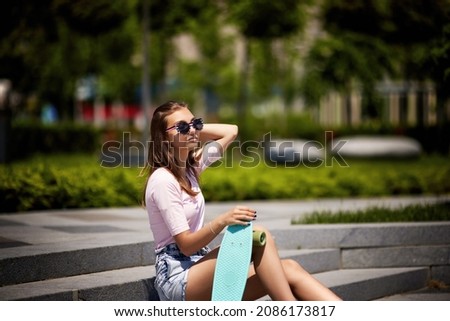 beautiful skateboarder girl with skateboard sitting outdoors