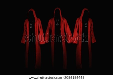 Group of mystery people in a red hooded cloaks.  Unrecognizable person. Hiding face in shadow. Ghostly figure. Satanic sect member. Conspiracy concept. Isolated on black. Royalty-Free Stock Photo #2086186465