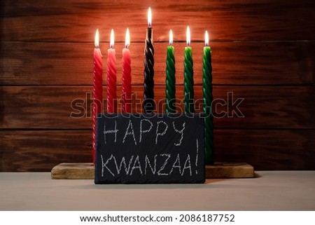 Happy Kwanzaa. African American holiday. Seven candles red, black and green on wooden background. Symbols of African heritage. Congratulatory inscription on chalk board.