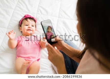 Loving young mom taking a picture of her cute baby with her smartphone to post it on social media 