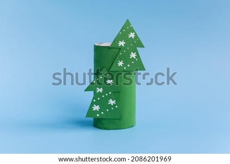 Holiday easy DIY craft idea for kids. Toilet paper roll tube toy Christmas tree on blue background. Creative New Year and xmas decoration eco-friendly, reuse, recycle handmade minimal concept