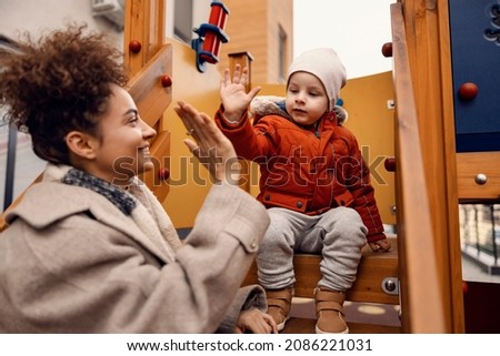 Kindergarten child giving high five to nursery governess on a playground. A cute little boy is sitting in a castle on a playground and giving a high five to his nursery governess. Royalty-Free Stock Photo #2086221031
