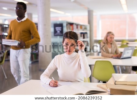 Portrait of positive woman with book in public library. High quality photo