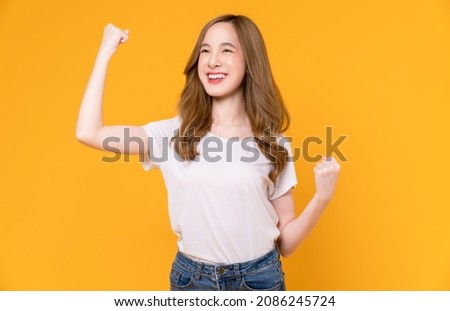 Beautiful Asian woman in a white t-shirt raises arms and fists clenched with shows strong powerful, celebrating victory expressing success.