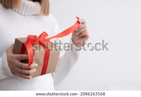 A woman in a white sweater untied the ribbon on the gift. layout with copy space and text space. High quality photo