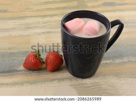 Hot white chocolate with pink strawberry marshmallows in blue mug with fresh strawberries