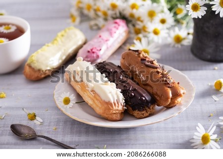 Beautiful delicious french eclairs set with original cream decor on white plate on  wooden background. Selective focus. Tasty colorful dessert profiteroles. Royalty-Free Stock Photo #2086266088