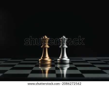 Golden and silver queen chess pieces standing together on a chessboard on dark background. Leader, team, enemy, cooperation, partnership, and business strategy concept. Royalty-Free Stock Photo #2086272562