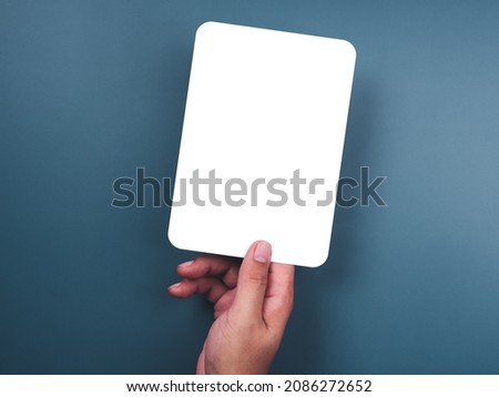 Mockup paper holding with the right hand. Hand holds the white blank mock-up white paper with a rounded corner and a vertical style on a blue background.