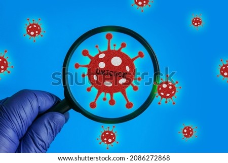 Hand wearing a blue glove holding a magnifying glass pointing on a Omicron variant of coronavirus.