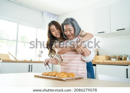 Asian lovely family, young daughter look to old mother cook in kitchen. Beautiful female enjoy spend leisure time and hugging senior elderly mom bake croissant on table in house. Activity relationship Royalty-Free Stock Photo #2086279078
