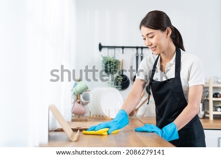 Asian young cleaning service woman worker clean kitchen table at home. Beautiful young girl housekeeper cleaner feel happy and wiping messy dirty cooking counter for housekeeping housework or chores. Royalty-Free Stock Photo #2086279141