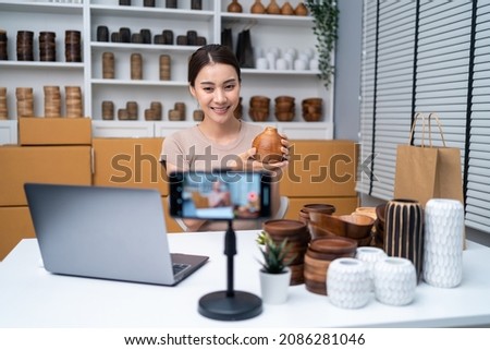 Asian beautiful woman sell vase product online live streaming at home. Young attractive girl use laptop computer shows goods to customer and present detail. Remote buying and purchase shopping concept