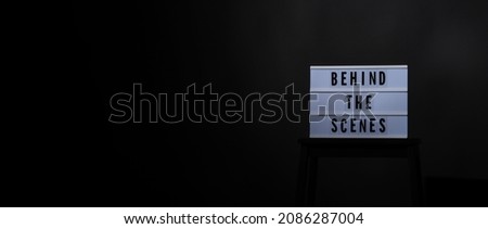 Director chair with behind the scene banner light box. Letterboard text Lightbox or Cinema Light box. Movie clapperboard and Director chair. Black Background. Represent video behind the scenes is on.