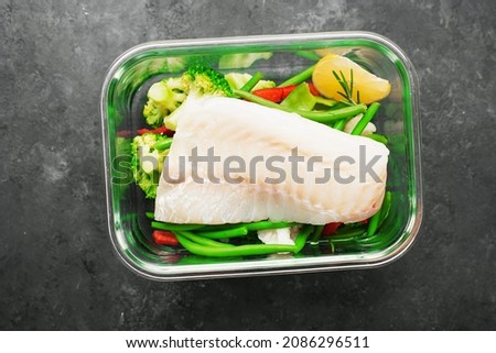 White cod fish fillet box. Fresh vegetables with a slice of cod in a glass container. Top view
