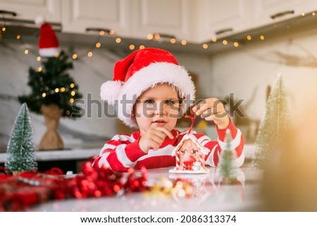 Christmas picture with a toy house and a child in a Santa hat.