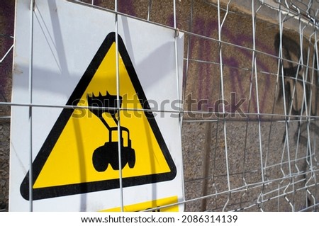 Heavy machinery at work warning sign. Tractor front loader draw visible throught the fence