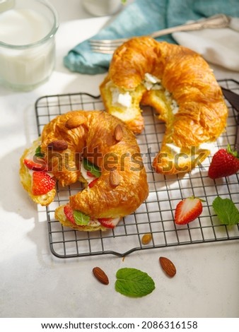 Delicious nutritious breakfast for two. Fragrant croissants with butter, fresh strawberries, almonds and green mint leaves on a metal wire rack. In the background is milk. White background. Romance.