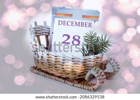 Calendar for December 28: leaves of a calendar with the name of the month, number 28 in a decorative sleigh, a spruce branch on a light background, close-up