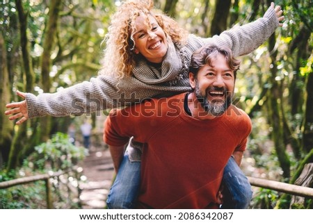 Overjoyed adult couple have fun together at outdoor park in leisure activity. Man carrying woman in piggyback and laugh a lot. Love and life mature people lifestyle concept. Enjoying vacation nature Royalty-Free Stock Photo #2086342087