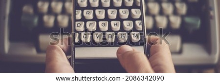 Close up of hands texting and writing on an old typewriter keyboard on modern mobile phone. Concept of technology and life in banner header picture