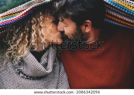 Couple in love kissing under a colorful woolen blanket. Concept of mature people in relationship and life forever. Man kiss woman with romance. Enjoying life with love Royalty-Free Stock Photo #2086342096