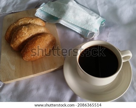 quick whole wheat bread on wooden board and black coffee white cup in rush hour during New Normal Life Covid19 and face mask on white sheet table