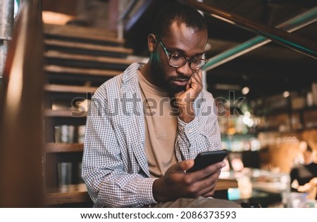 Millennial dark skinned male blogger using 4g wireless on cellular device for making online booking and banking, young black man in eyewear checking received email message on smartphone gadget