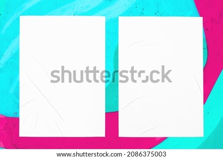 Closeup of colorful messy painted urban wall texture with two wrinkled glued poster templates. Modern mockup for design presentation. Creative pink mint green blue urban city background. 