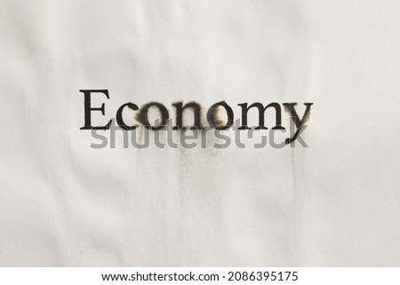 Word "ECONOMY" is written on a paper background with with traces of water. Concept of economy falling and savings