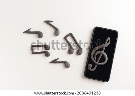 Smartphone phone with treble clef on display and musical notes on white background. Apps to listen music on your phone Royalty-Free Stock Photo #2086401238