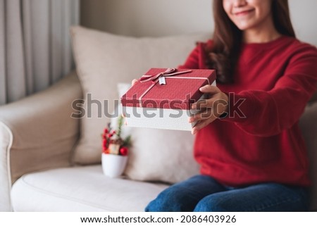 Closeup image of a young woman holding and giving a red present box 