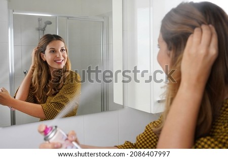 Young woman applying dry shampoo on her hair before going out. Fast and easy way to covering grey hair with instant spray dye. Royalty-Free Stock Photo #2086407997