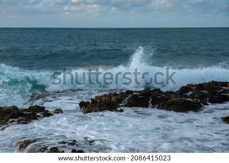 Turquoise sea stone beach, breaking waves on a cloudy spring day. Beautiful sea background. The concept of summer, vacation, travel. The purest clear sea water, large stones on the beach close-up