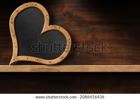 Blank blackboard with wooden frame in the shape of a heart, on top of a wooden shelf with copy space.