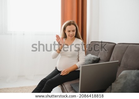 Pregnant woman video chatting with family on laptop waving hand to screen
