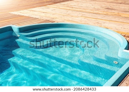 New modern fiberglass plastic swimming pool entrance step with clean fresh refreshing blue water on bright hot summer day at yard or resort hotel spa area. Wooden flooring deck of teak or larch board Royalty-Free Stock Photo #2086428433