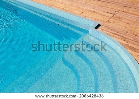 New modern fiberglass plastic swimming pool entrance step with clean fresh refreshing blue water on bright hot summer day at yard or resort hotel spa area. Wooden flooring deck of teak or larch board Royalty-Free Stock Photo #2086428436