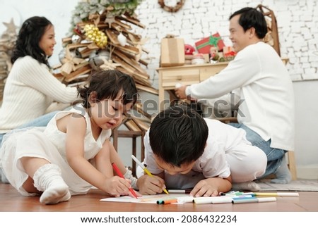 Small children drawing pictures on the floor when their parents decorating Christmas tree