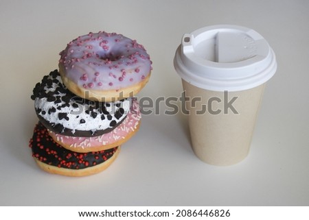 Colorful donuts and paper cup on white table, close up. Tower of donuts and coffee paper cup. Blank  disposable coffee paper cup with donuts on white tabletop. Coffee shop idea