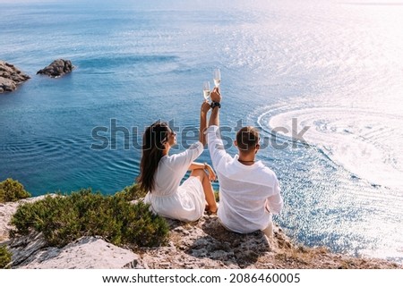 A couple in love celebrates their engagement on the seashore. A beautiful couple drinks champagne by the sea. Honeymoon trip. Lovers on the beach. Wedding travel. Couple on vacation. Copy space Royalty-Free Stock Photo #2086460005