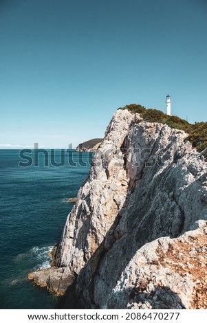 Ionian sea island steep rocky cliffs with lighthouse on top in greenery. Bright clear blue sky summer day in Greece. Scenic travel destination. Lefkada island. Vertical, color graded